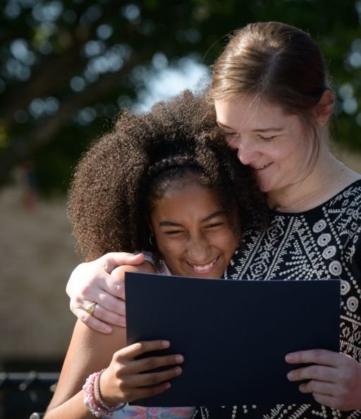 A young student and teacher smiling, both holding a black card, embracing.